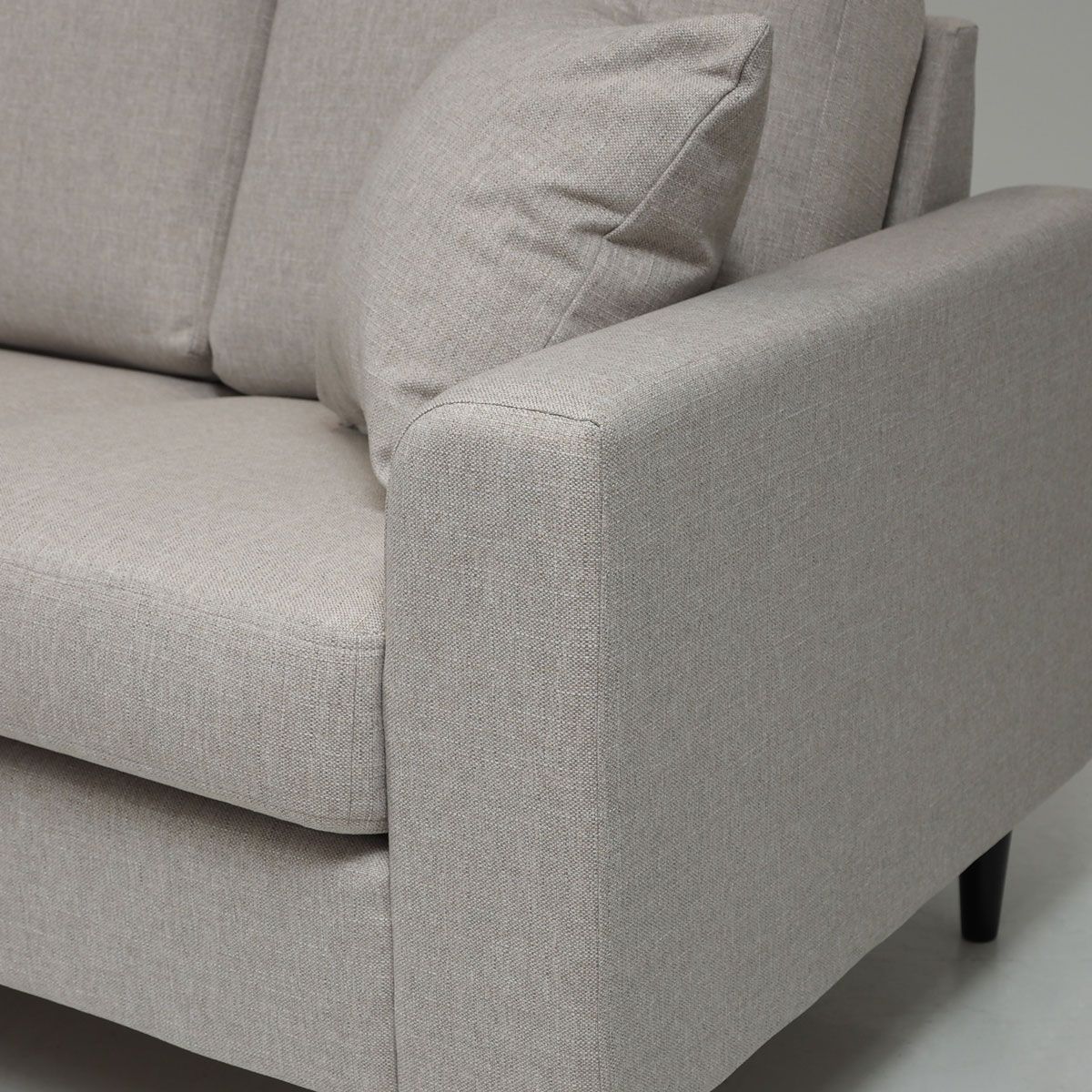 Kuva beigen Napue sohvan käsinojasta, joka on yläreunasta muotoiltu pyöreäksi ja siksi siihen voi nojata päällä sohvalla maatessa