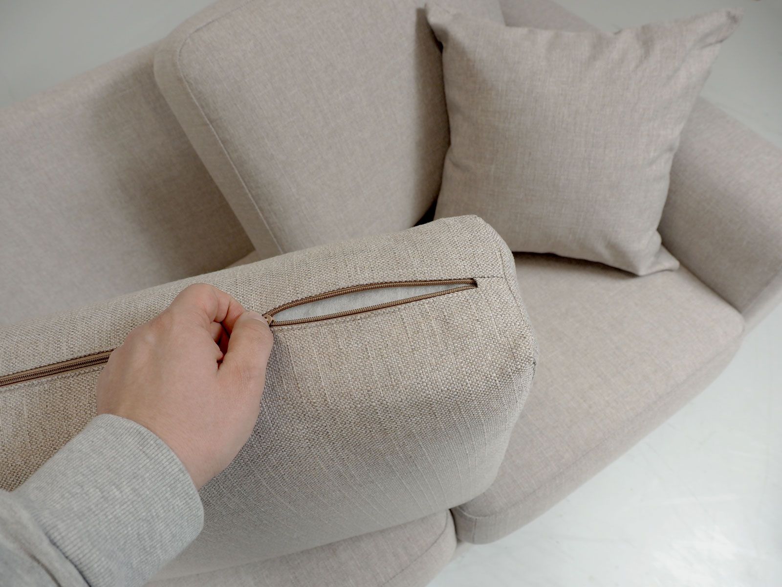 Kuva, jossa käsi avaa divaanisohvan istuintyynyn vetoketjua havainnollistaen, että sohvan tyynyistä saa irrotettua päälliskankaat.