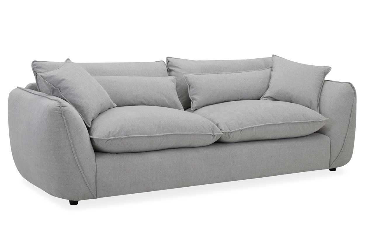 Muhkea 3,5-istuttava sohva harmaalla kangasverhoilulla. Muhkeat irtotyynyt sekä koristetyynyt.